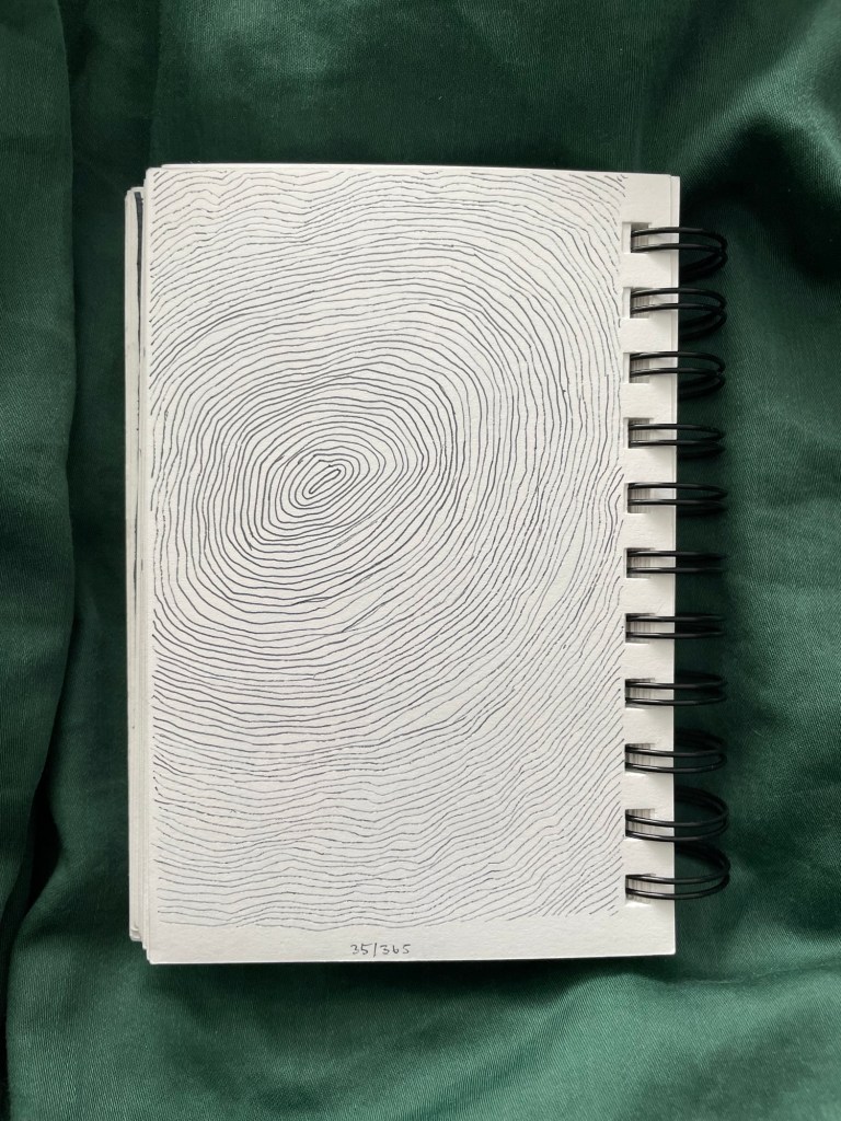 Wire bound sketchbook with line drawing on the open page, laying on top of green fabric